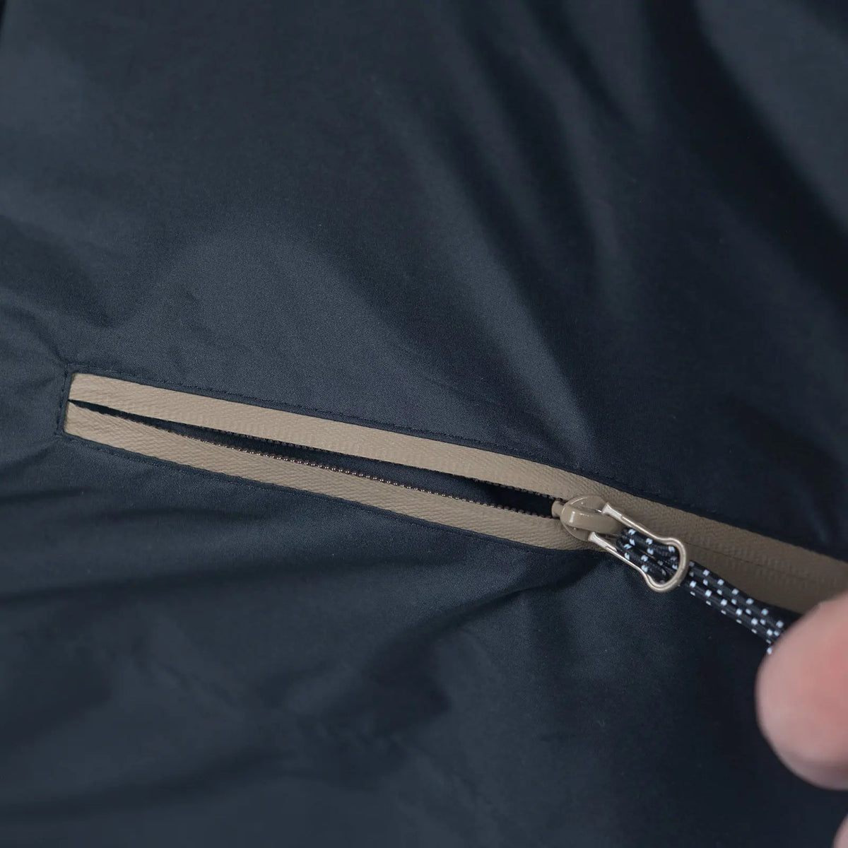Main utilisant la fermeture éclair imperméable de la poche latérale de la veste Baja Coastline, conçue pour ranger l’essentiel lors des promenades pluvieuses.