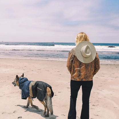 Chien portant le poncho imperméable Baja Coastline, debout sur la plage avec son maître et contemplant l’océan, prêt pour toutes les aventures côtières.